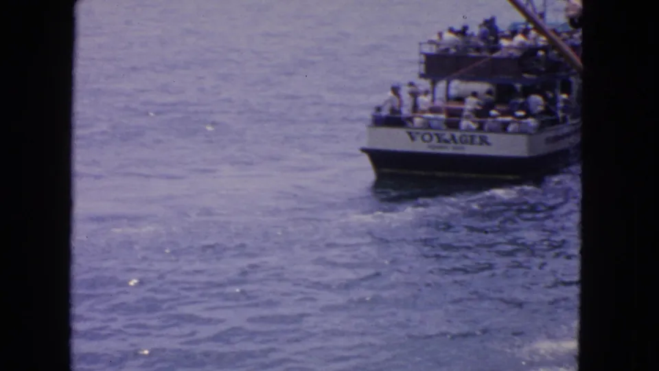 Home-movie frame showing the VOYAGER boat with passengers, partly blocked by a dark vertical film edge.