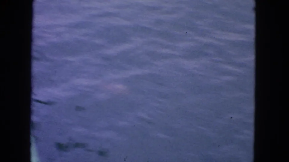 1963 San Francisco 8mm frame of calm water with dark bridge or railing edge at the side and no identifiable people or landmarks.