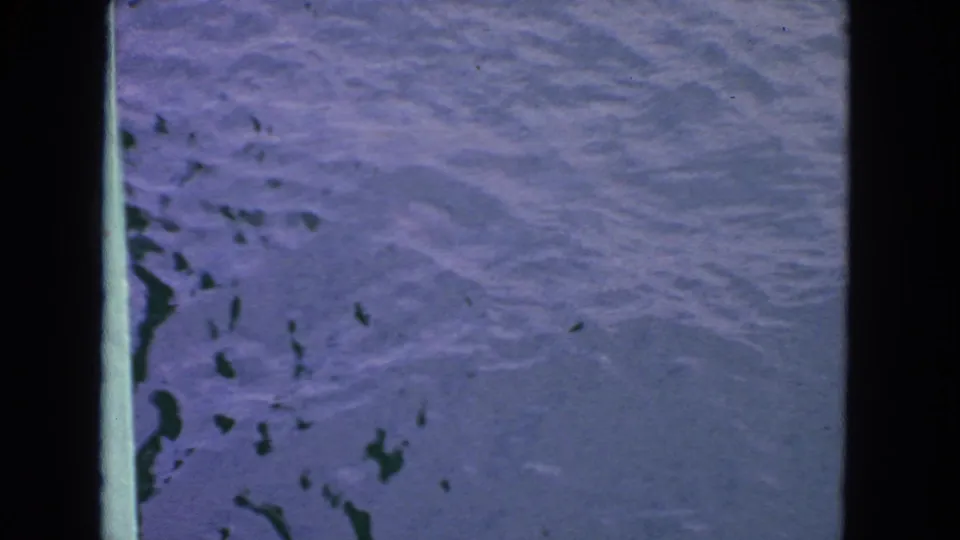 1963 San Francisco 8mm frame showing blue rippling water, scattered dark debris, and a central bridge or railing support.