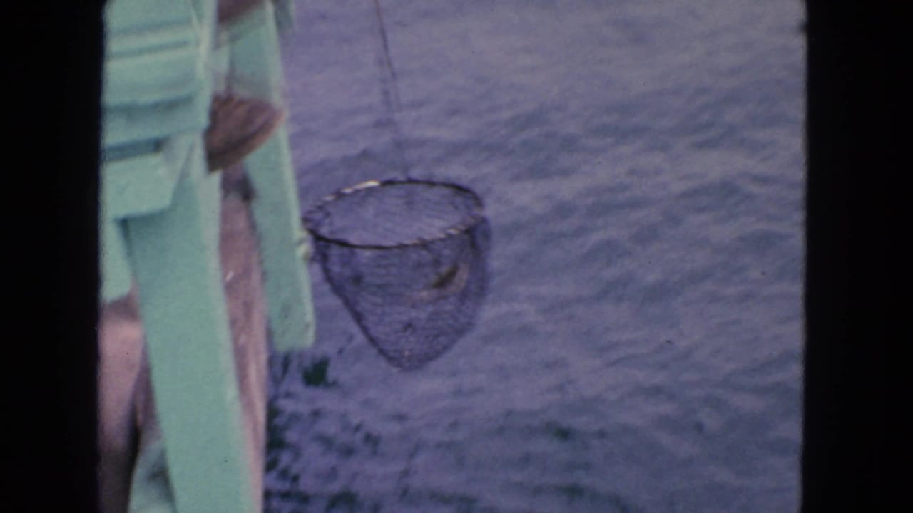 1963 San Francisco home-movie frame showing a fishing net hanging beside a green dock or boat edge over the water.