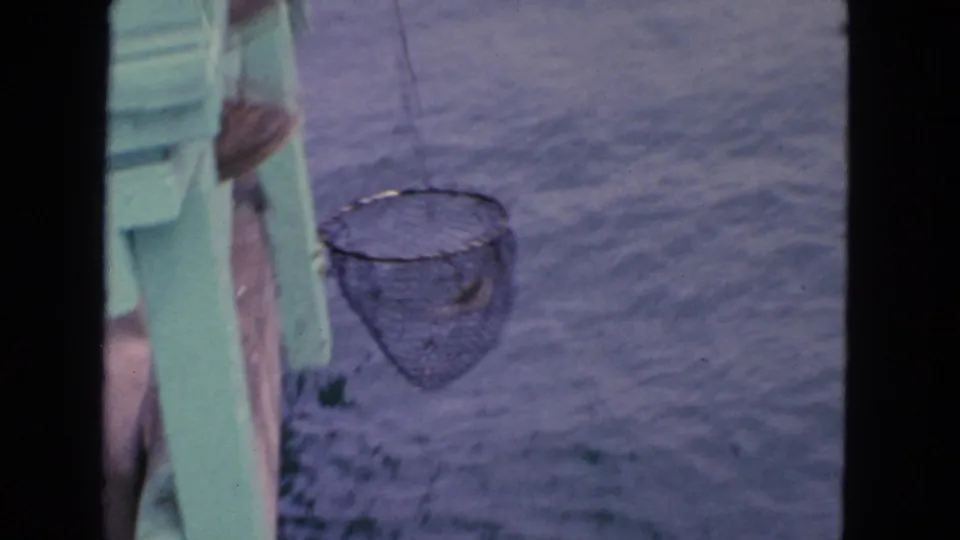 1963 San Francisco home-movie frame showing a fishing net hanging beside a green dock or boat edge over the water.