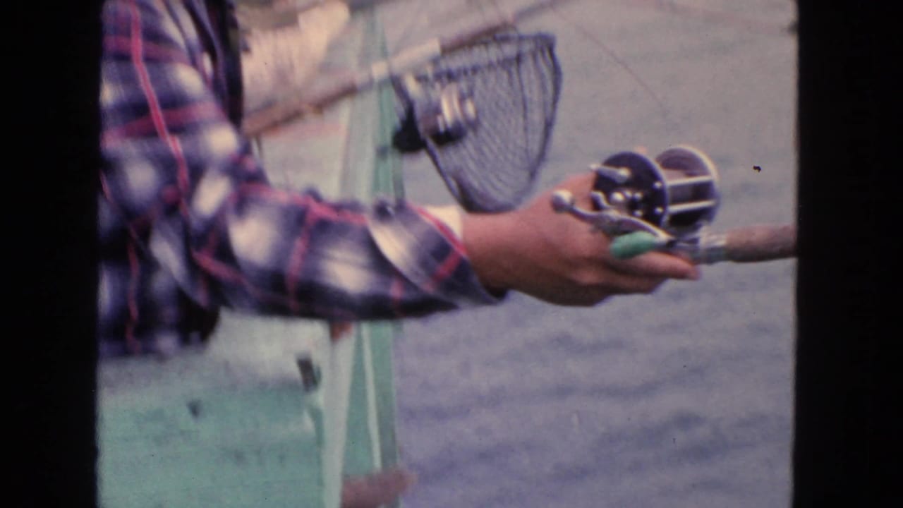 A plaid-shirted fisherman handles a rod and reel near the waterfront in this 1963 San Francisco home-movie frame.