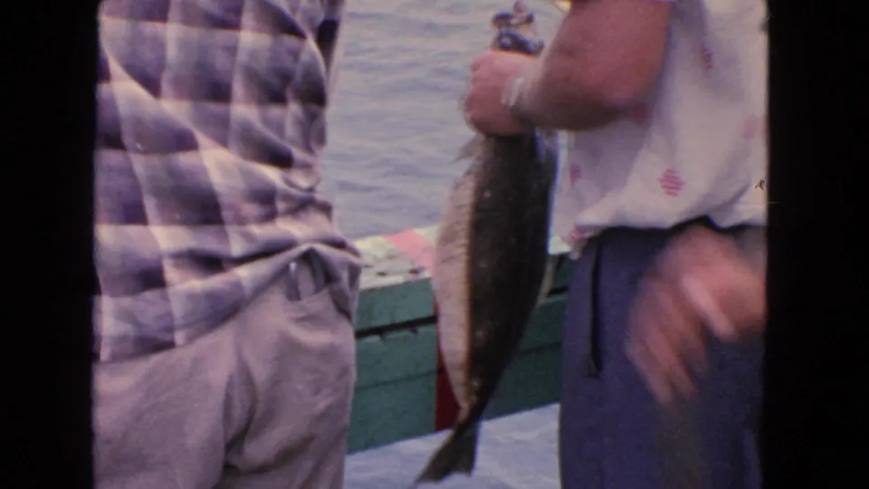 A freshly caught fish is held up near the water, with adults partly visible in a 1963 San Francisco fishing scene.