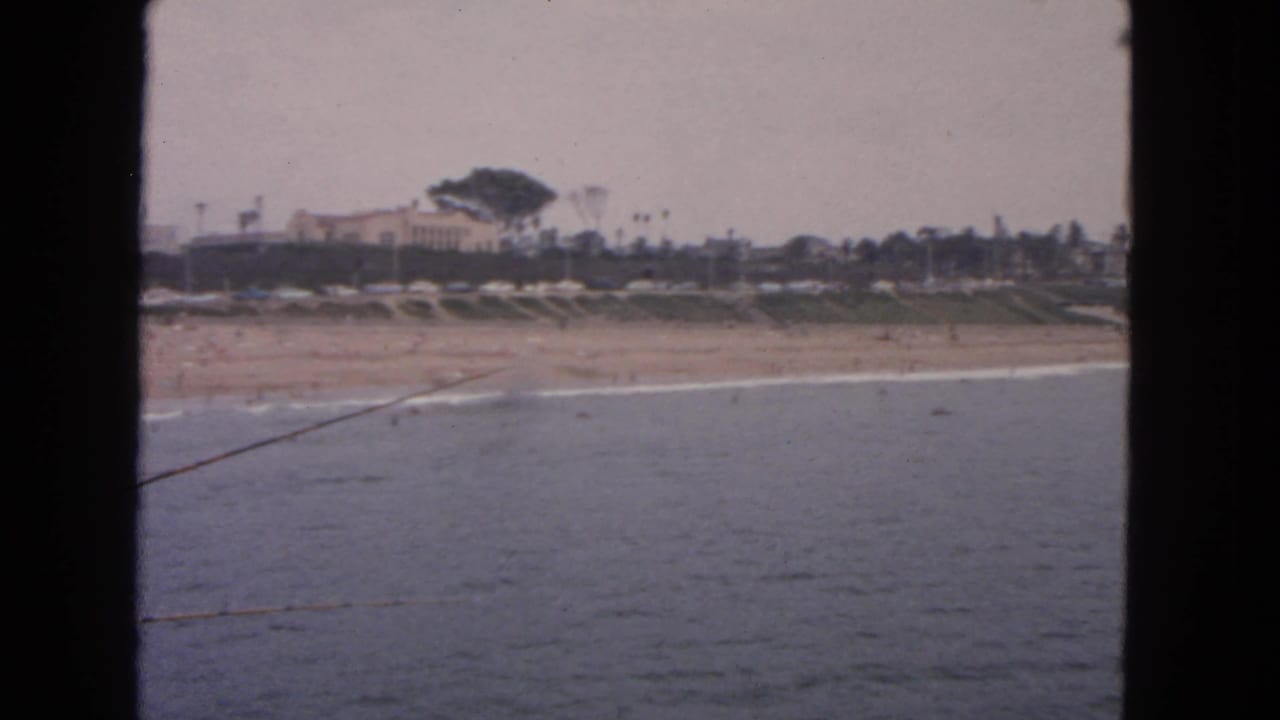 1963 San Francisco coastal view from water toward a beach, low buildings, and scattered palms.