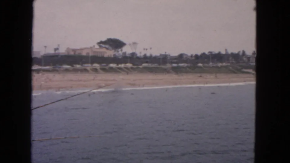 1963 San Francisco coastal view from water toward a beach, low buildings, and scattered palms.
