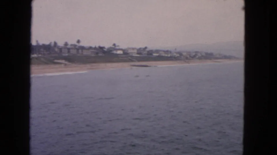 Wide 1963 San Francisco shoreline view with water foreground, sandy beach, and distant houses.