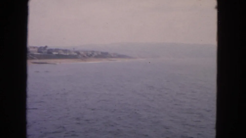 Faded 8mm frame of the San Francisco-area coastline, with ocean in the foreground and homes along a hazy beach ridge.