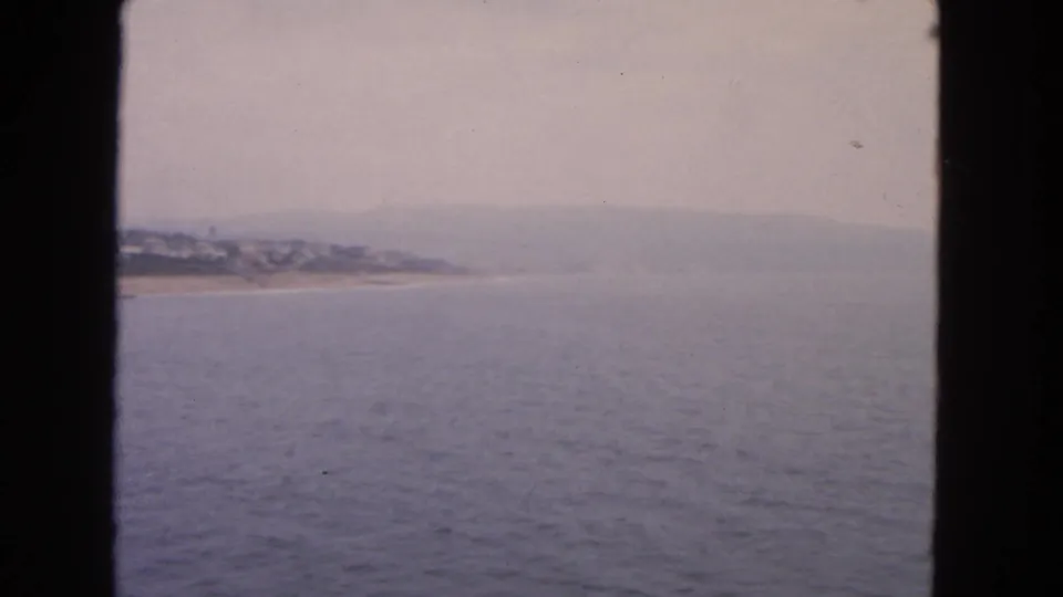 End of the 1963 8mm coastal panorama, showing open water, a faint beach curve, and distant San Francisco-area hillside homes.