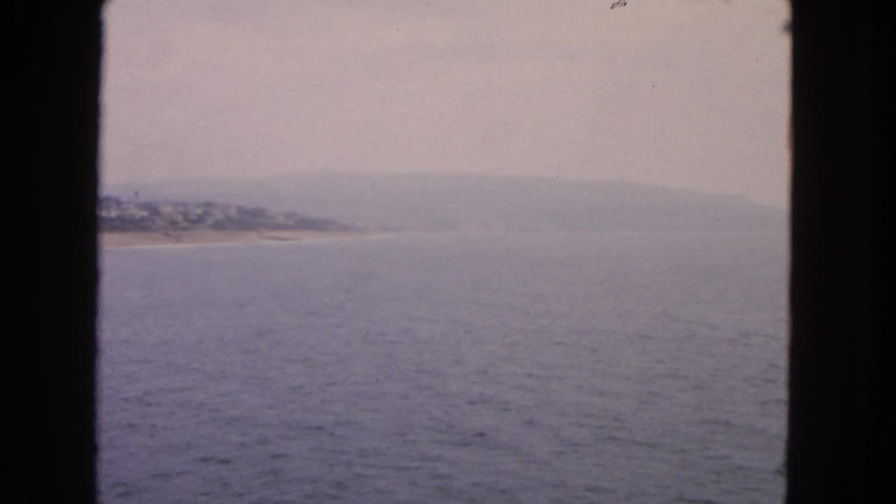 Distant shoreline and low hills across calm water, framed by dark vessel window edges.