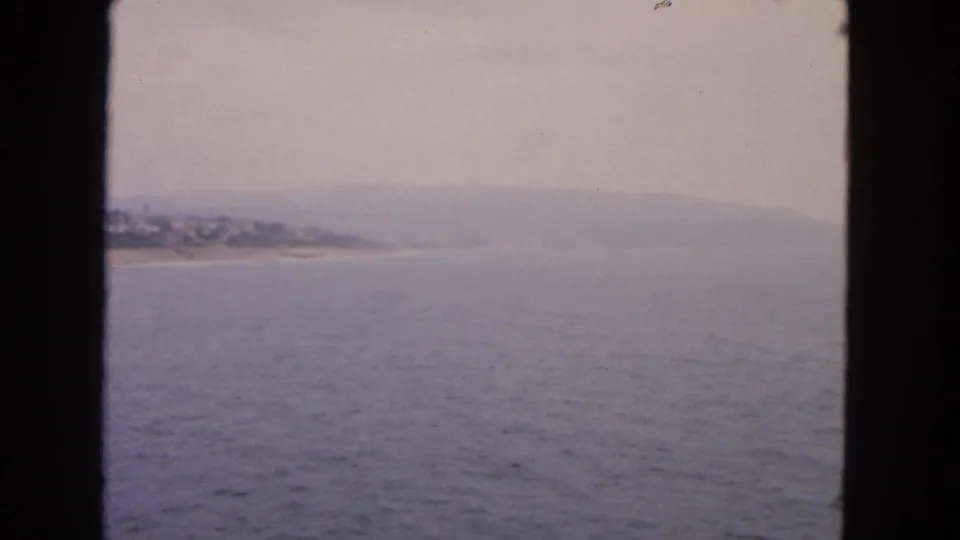 1963 San Francisco Bay home-movie view of calm water, hazy shoreline, and low hills seen through dark window framing.