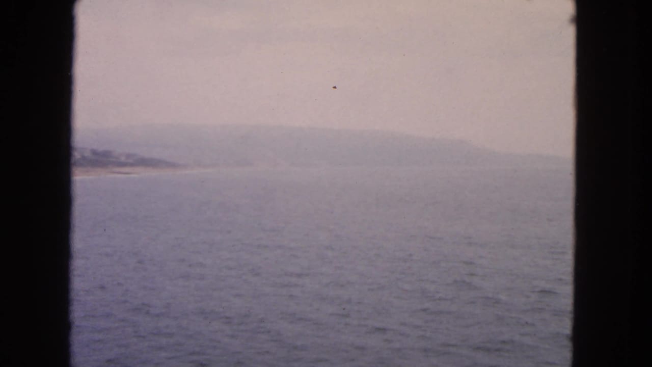 Open water with a hazy coastline and low hills, divided by dark window framing.