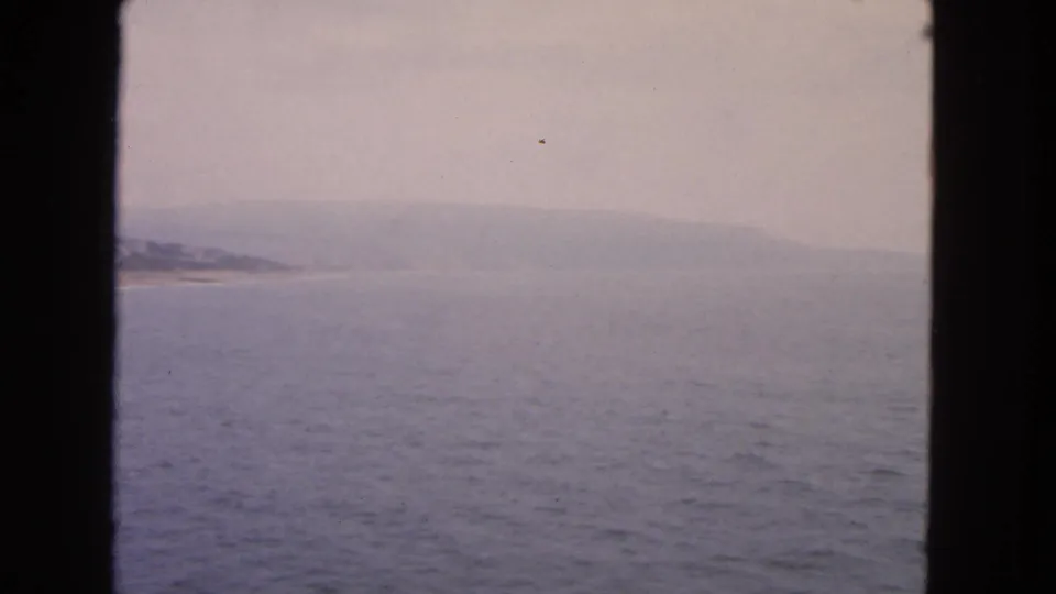 A 1963 San Francisco Bay vessel-window view shows blue-gray water, distant coast, low hills, and soft overcast haze.