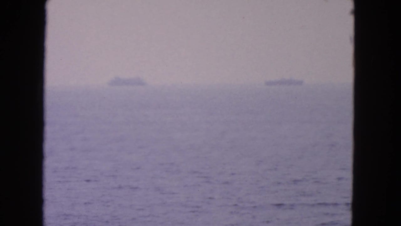 Soft, hazy ocean horizon with distant ships framed by dark vertical film edges.