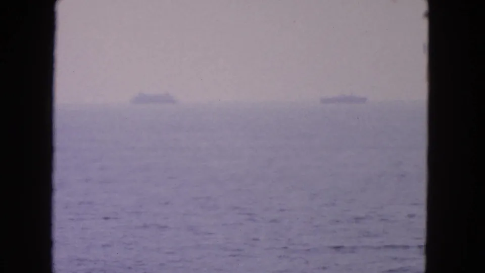 1963 8mm home-movie frame showing a blurred ocean horizon near San Francisco with small distant ships and dark frame edges.