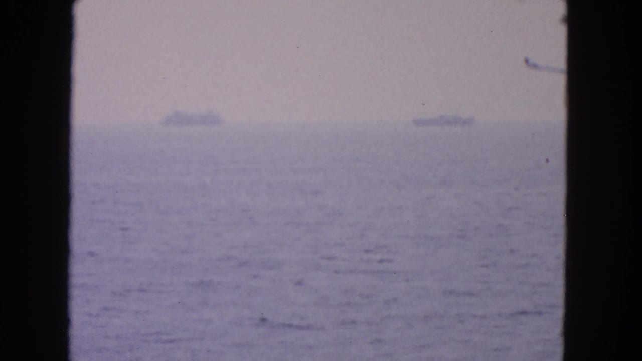 Blurred ocean and sky with distant ships separated by a dark central frame bar.