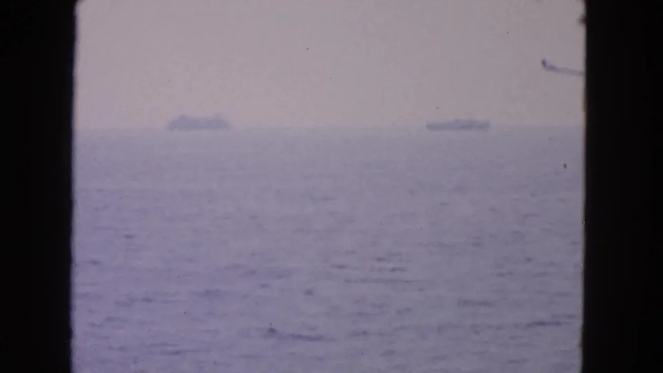 Soft 1963 coastal 8mm view with distant ships on the horizon and a dark vertical divider through the frame.