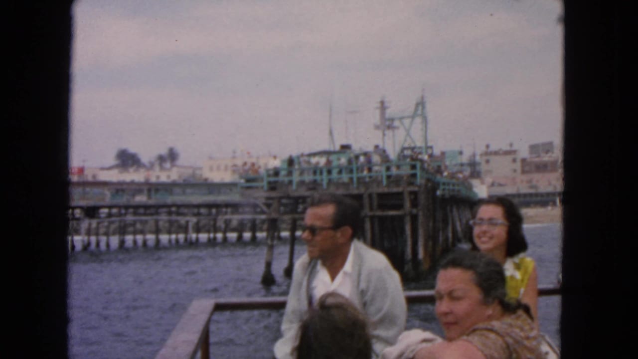 Adults seated on a boat with a pier and waterfront buildings behind them.