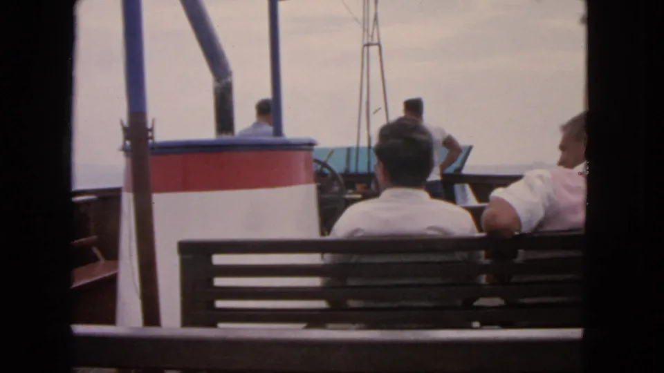 1963 San Francisco home-movie frame showing men seated on a boat deck, viewed from behind beside cabin trim and railings.