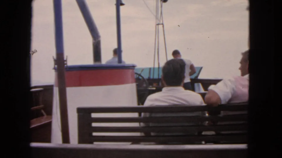 Home-movie view from a 1963 San Francisco boat trip showing seated adult men on deck under an overcast sky.