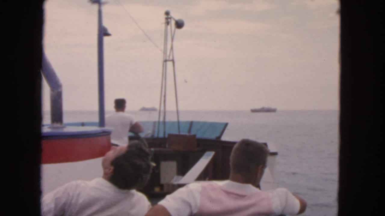 Men aboard a small boat look toward open water with a distant ship on the horizon.