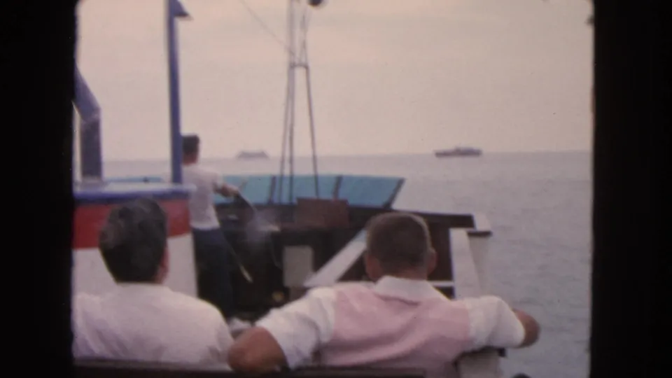 1963 San Francisco home-movie frame of men on a small boat, with open bay water and distant ships visible.