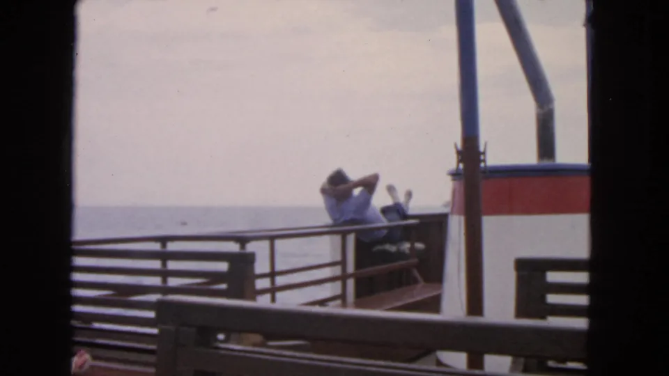 1963 San Francisco home-movie frame of a man resting on a boat deck, with railings, vessel structure, and open water visible.