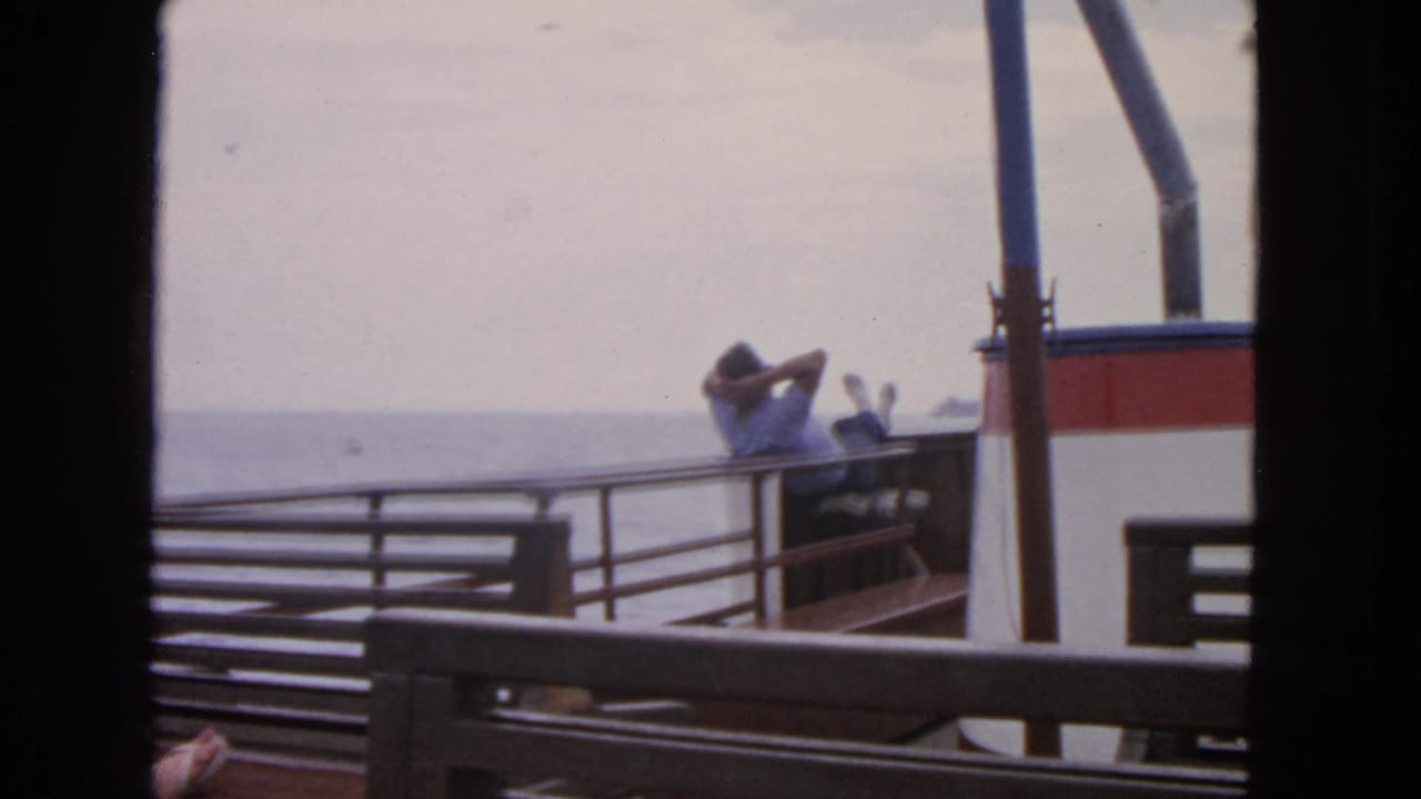 1963 San Francisco home-movie frame showing men on a small boat deck watching a larger ship offshore.