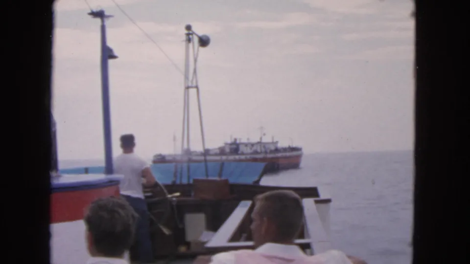 Men in light shirts watch a larger vessel from the deck of a small boat in 1963 San Francisco footage.