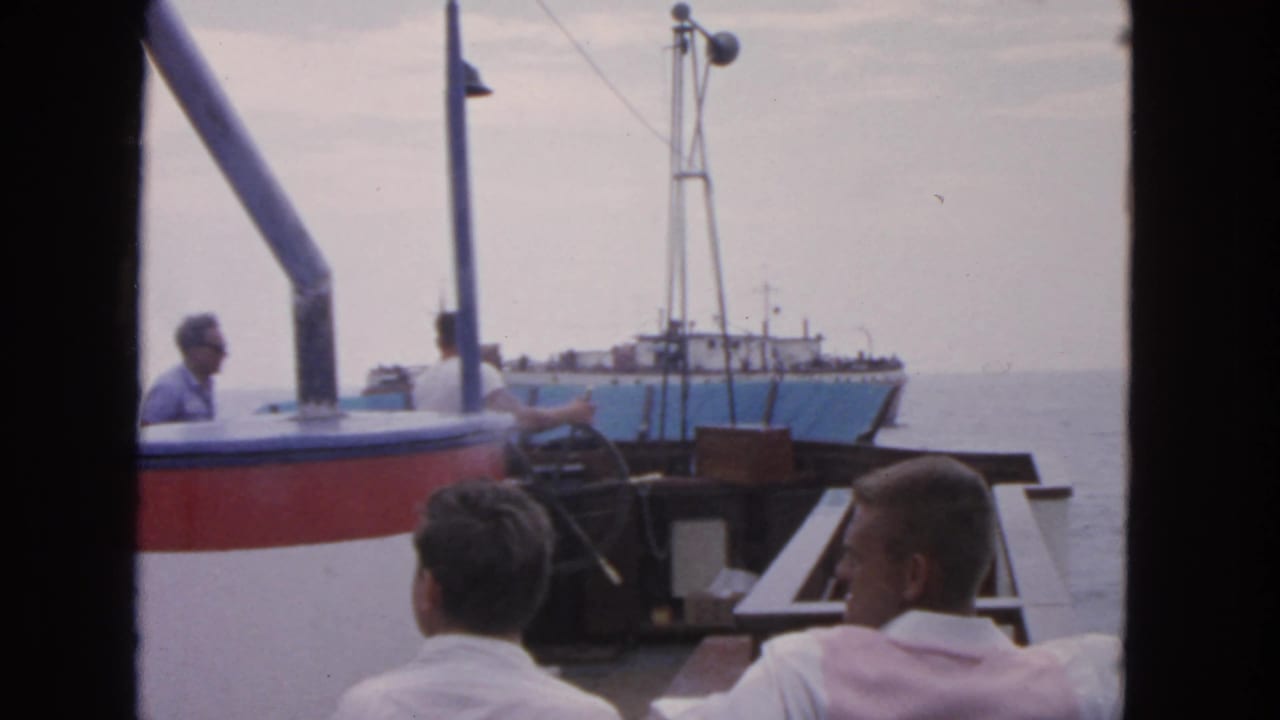 Men on a boat deck face a nearby blue-and-white vessel on the water.