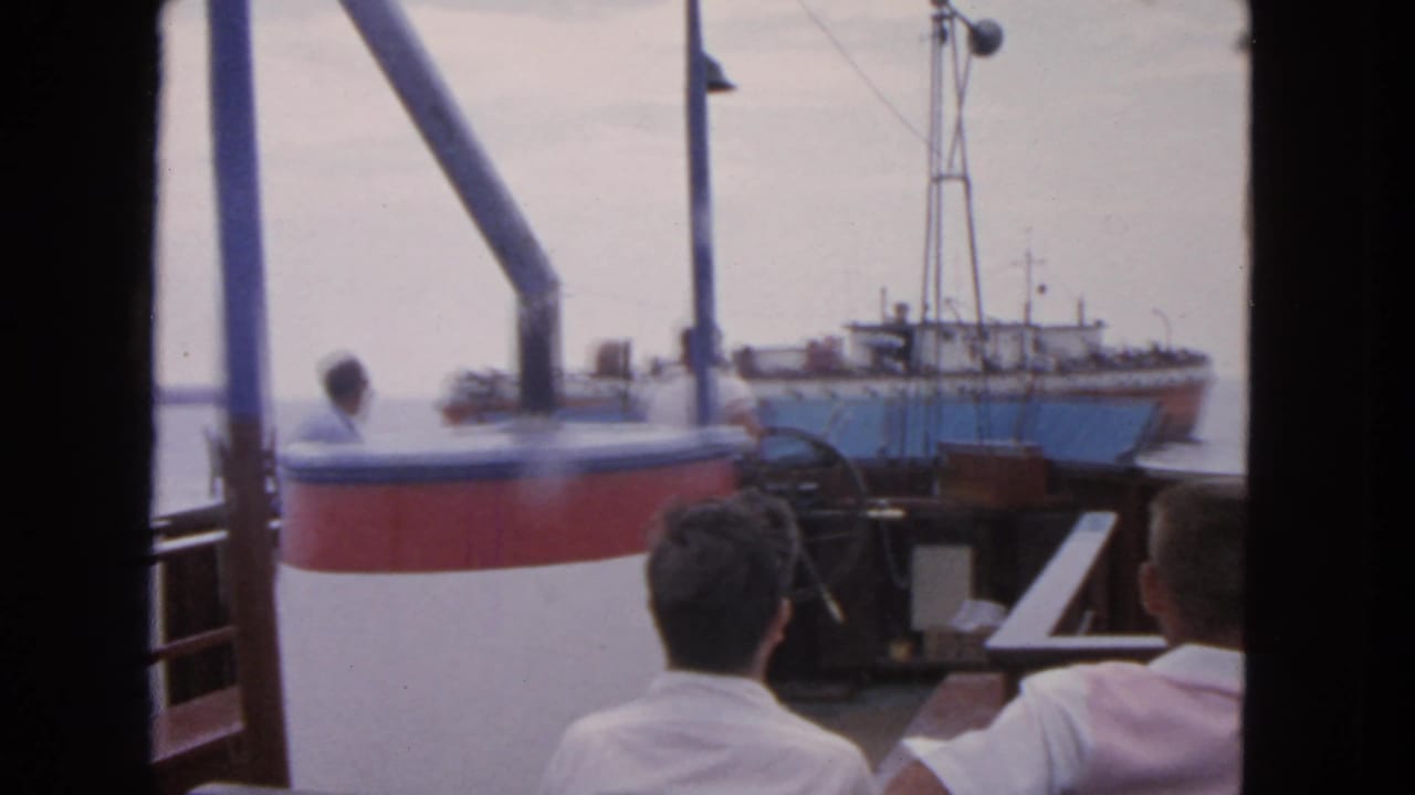 Men on a boat deck face the water near a large fishing vessel.