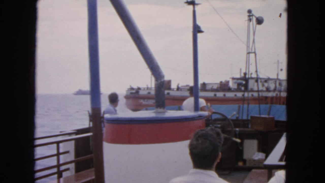1963 San Francisco boating frame with a man near the helm and a fishing vessel visible beyond the boat railing.