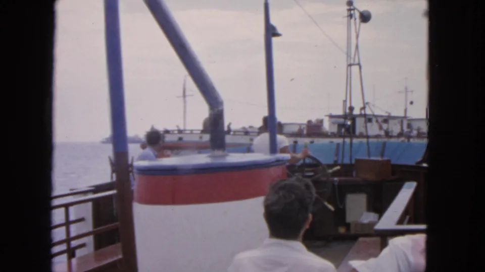 1963 San Francisco home-movie view from a boat deck with seated passengers, railings, and a fishing vessel beyond.