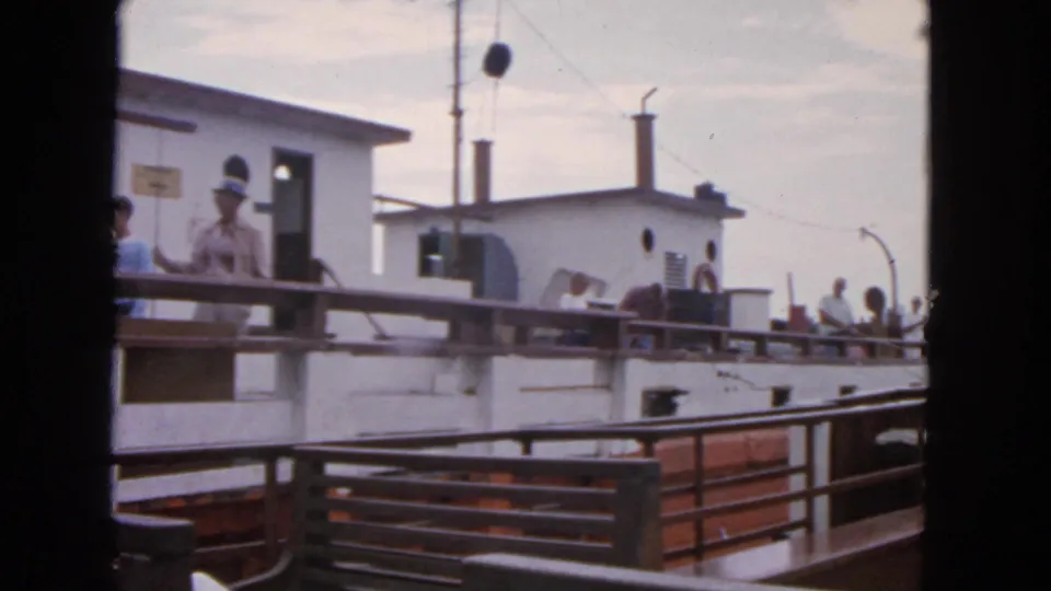 1963 San Francisco harbor footage showing passengers on a boat deck beside a white cabin, with railings, benches, and waterfront equipment visible.
