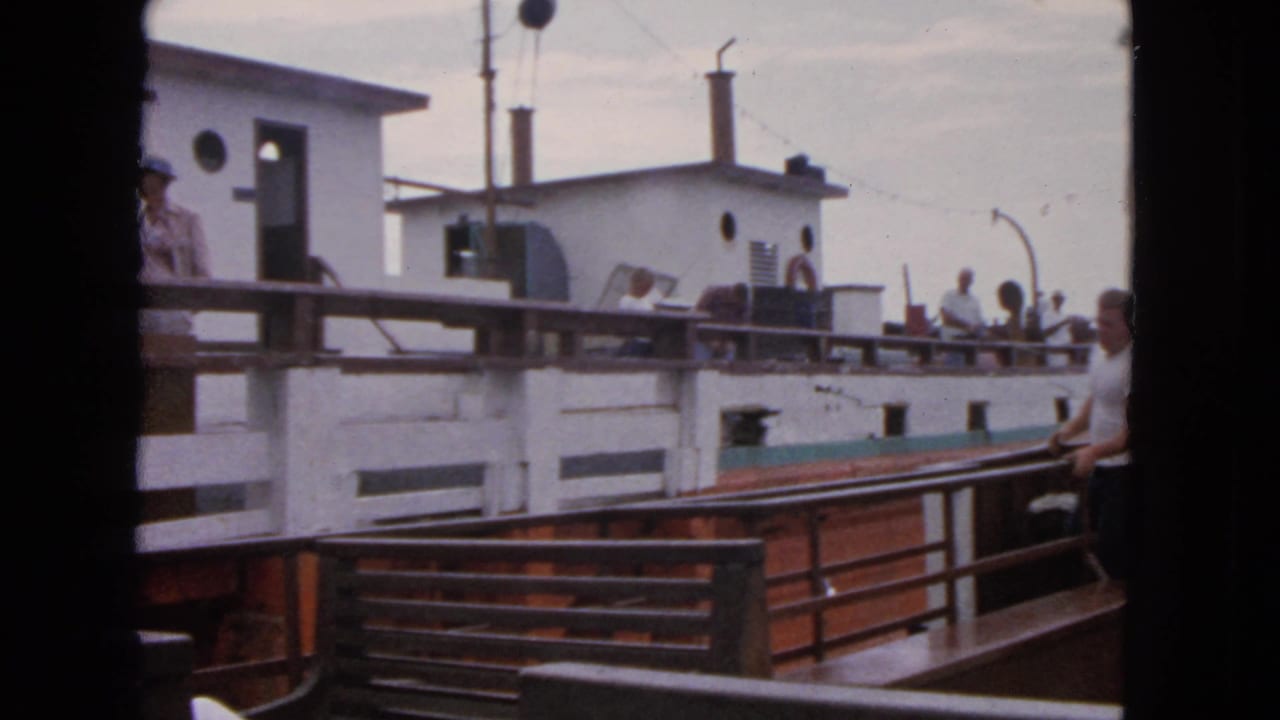 Two passenger boats close together with people standing on decks and railings in view.