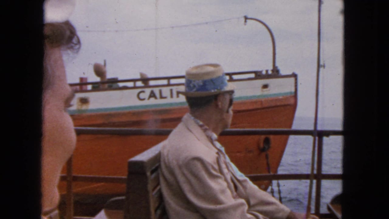 1963 San Francisco home-movie frame of seated ferry passengers watching an orange-and-white vessel marked CALIFORNIA pass nearby.