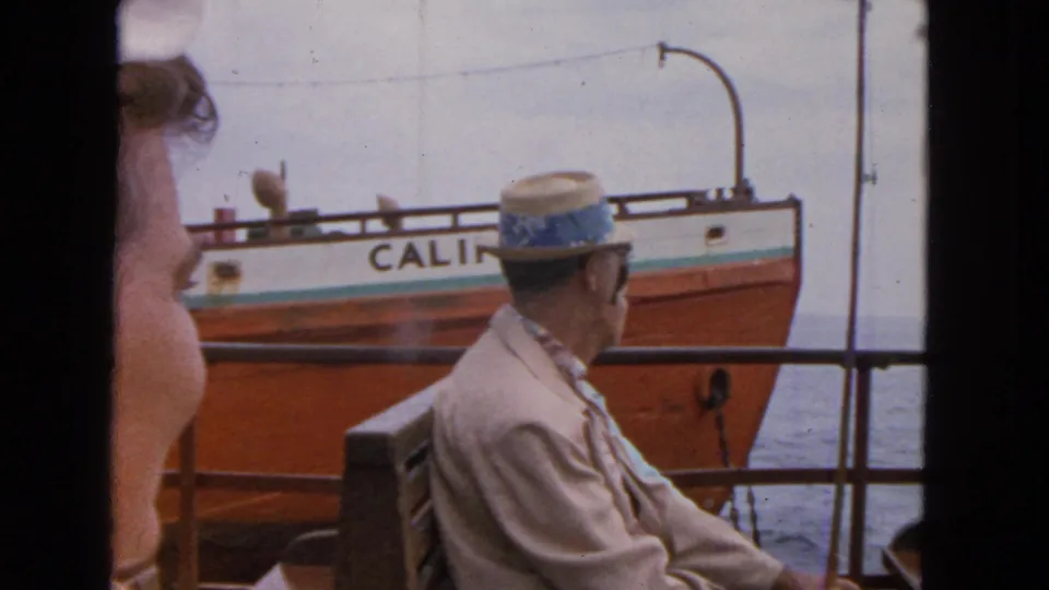 1963 San Francisco home-movie frame of seated ferry passengers watching an orange-and-white vessel marked CALIFORNIA pass nearby.