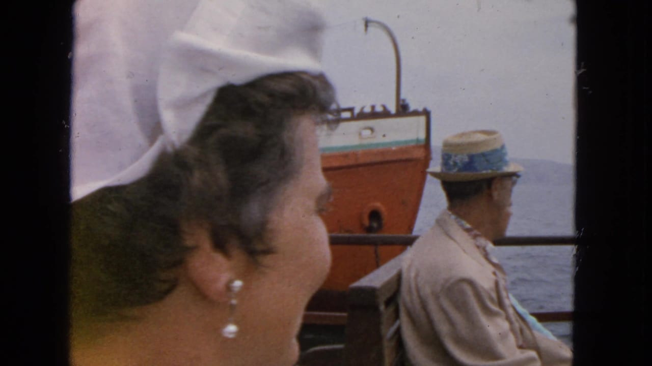 1963 San Francisco ferry view with a woman in a white headscarf and pearl earrings looking toward a passing vessel on the bay.