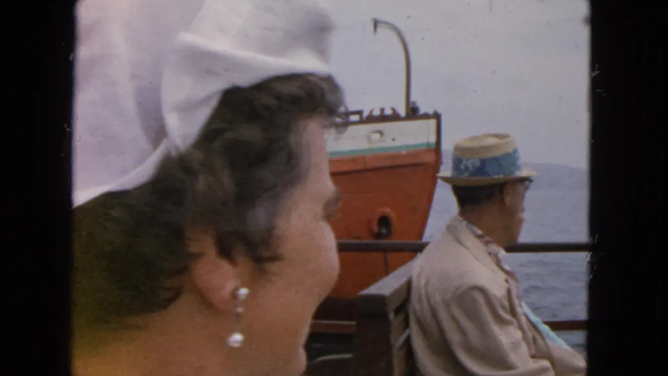1963 San Francisco ferry view with a woman in a white headscarf and pearl earrings looking toward a passing vessel on the bay.