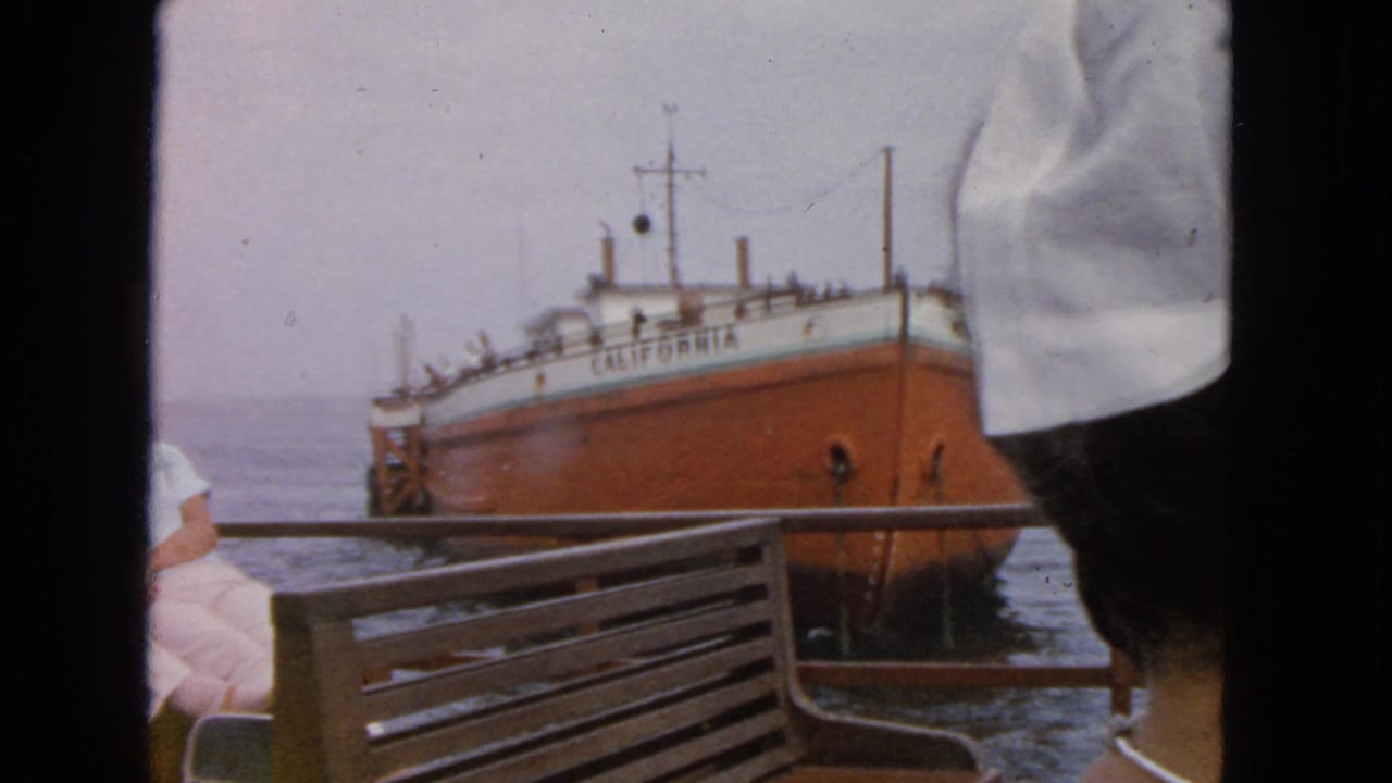 1963 San Francisco Bay home-movie frame with a woman partly visible on deck and the ship CALIFORNIA in the background.