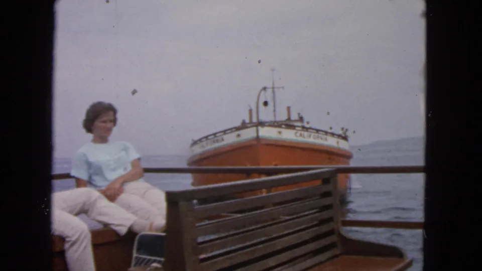 1963 San Francisco Bay frame showing a woman seated on deck while the orange-and-white ship CALIFORNIA floats behind her.