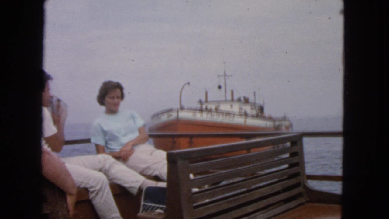 Adults seated on a boat deck with an orange and white ship in the distance.