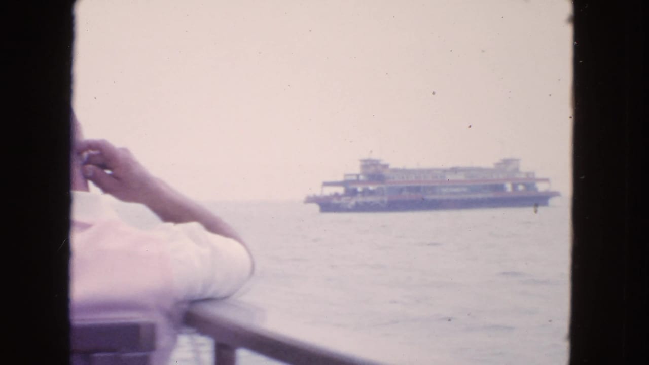 1963 San Francisco Bay frame showing a passenger at the rail with a distant ferry on the water under hazy light.