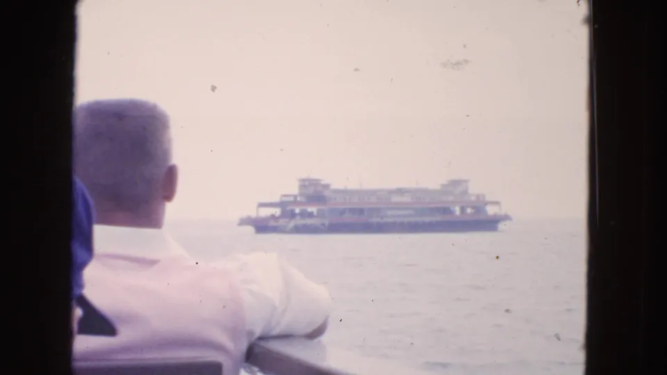 1963 San Francisco Bay frame with two passengers seen from behind as a distant ferry sits across the water.