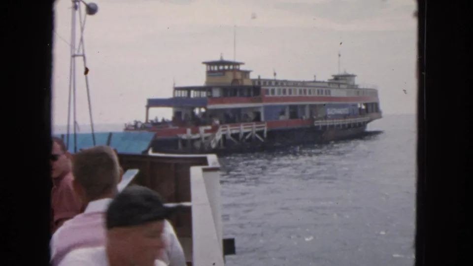 1963 San Francisco bay footage showing a multi-deck ferry closer in frame, with boat passengers and railing in the foreground.