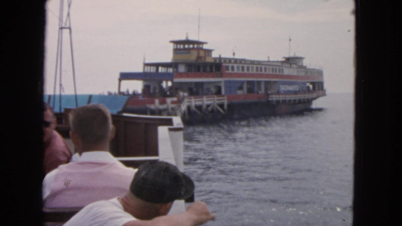 Passenger ferry approaches across water while seated people watch from another boat.