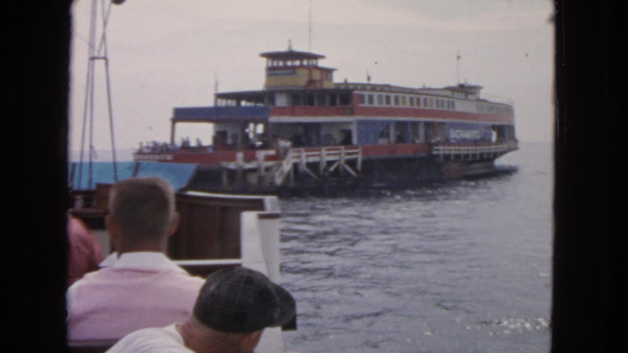 The ferry appears closer to the dock, with foreground passengers facing the water from another boat in San Francisco.