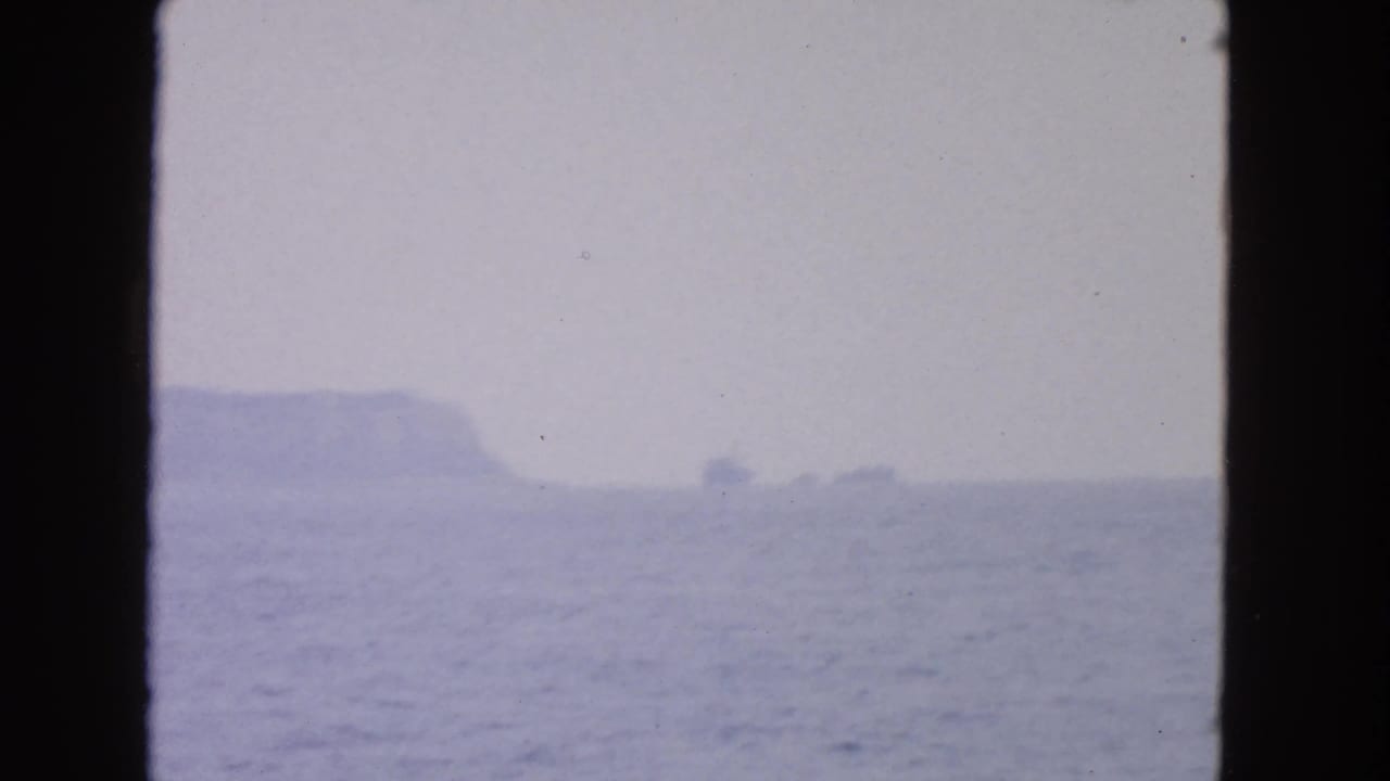 Hazy ocean view with distant rock formations under a pale cloudy sky.
