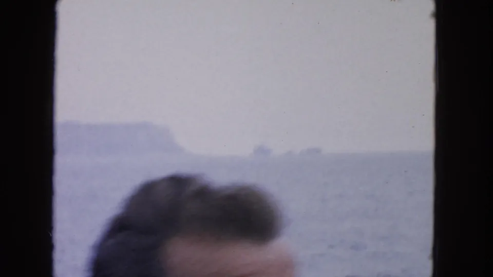 A partial passenger head appears low in the frame against a 1963 San Francisco-area seascape of water, haze, and rock formations.