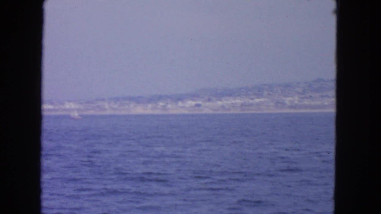 Blue water and a populated distant shoreline framed by dark vertical window edges.