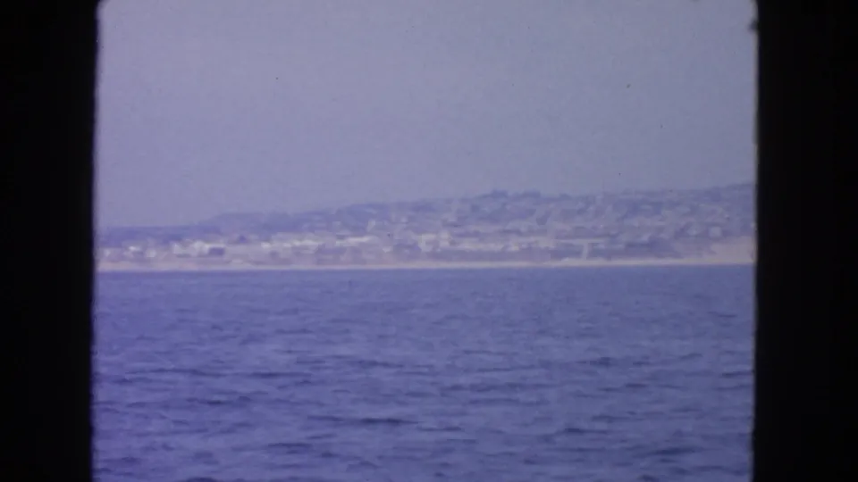 1963 home-movie view across San Francisco Bay toward a hazy shoreline with low buildings and hills beyond.